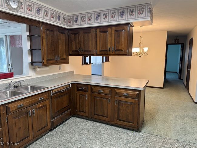Kitchen with a peninsula, light countertops, dark brown cabinets, pendant lighting, and a sink | Image 13