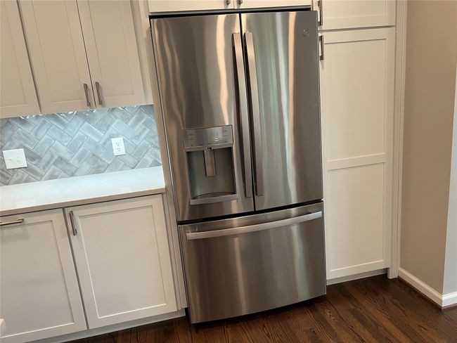Kitchen featuring stainless steel fridge with ice dispenser, dark wood-style floors, decorative backsplash, light stone countertops, and white cabinetry | Image 15