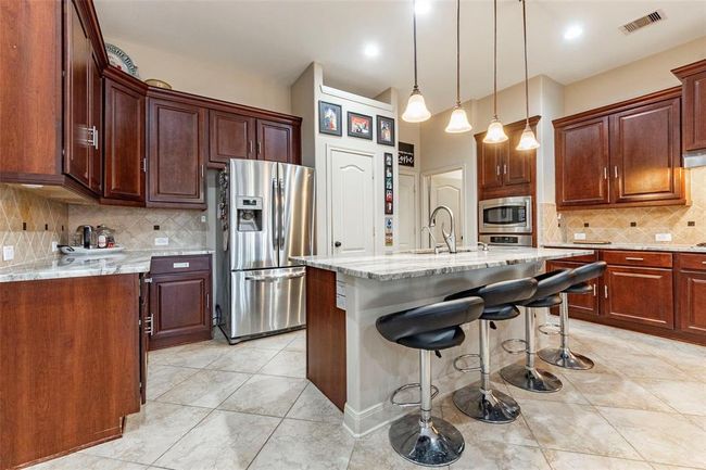 Large granite island with hanging bar lights and breakfast bar seating. Tile flooring throughout. | Image 23