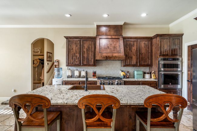 Kitchen featuring double oven, stone tile flooring, tasteful backsplash, light stone countertops, and ornamental molding | Image 14