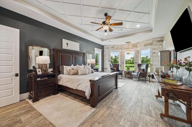 The oversized primary bedroom is a tranquil retreat, highlighted by a striking stone accent wall and meticulous attention to detail in the custom ceiling molding. Large windows offer breathtaking sunrise views, creating a peaceful and inviting atmosphere. | Image 5