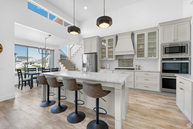 Kitchen featuring custom exhaust hood, stainless steel appliances, a kitchen breakfast bar, an island with sink, and decorative light fixtures | Image 9