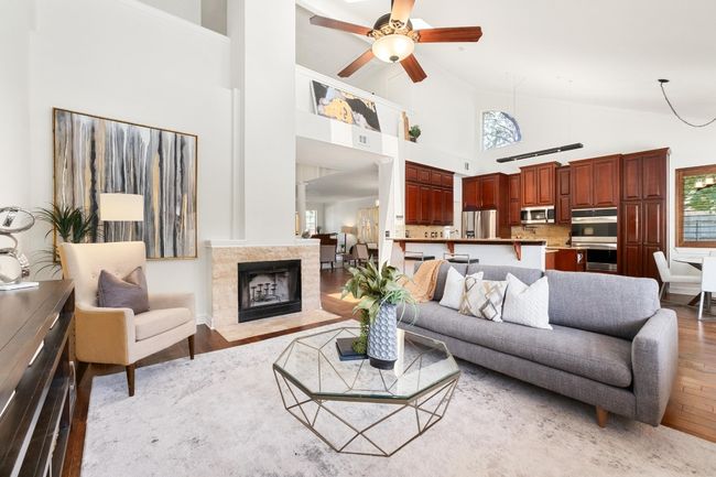 Living area with light wood finished floors, high vaulted ceiling, healthy amount of natural light, a ceiling fan, and a fireplace | Image 7