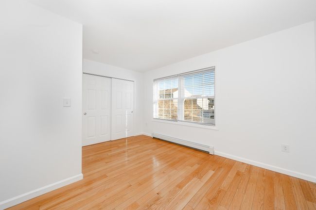 Unfurnished bedroom with a baseboard radiator, a closet, hardwood / wood-style flooring, and baseboards | Image 15