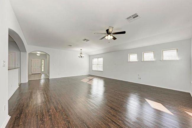Unfurnished living room with a ceiling fan, wood finished floors, arched walkways, a chandelier, and baseboards | Image 14