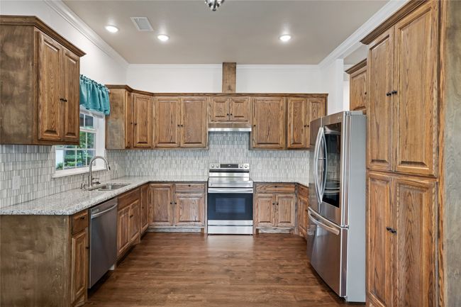 Kitchen with stainless steel appliances, under cabinet range hood, light stone counters, dark wood-type flooring, and decorative backsplash | Image 11