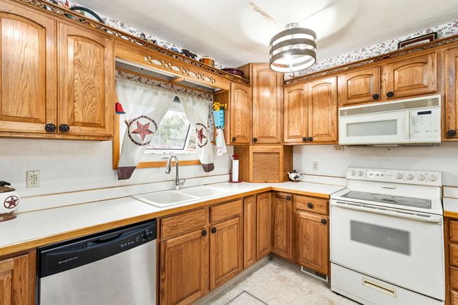 Kitchen with white appliances, light countertops, a sink, and brown cabinetry | Image 46