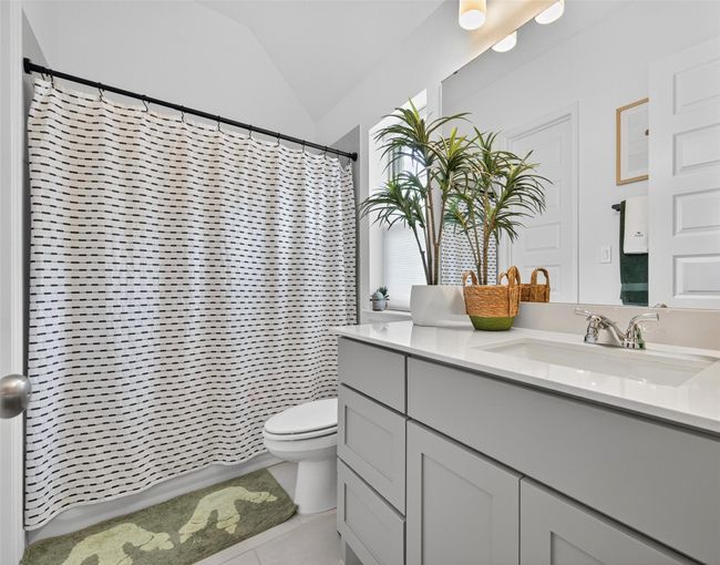 Full bathroom featuring a large vanity with shaker-style cabinetry, quartz countertop, and an undermount sink. Includes a shower/tub combo and tile flooring, all in a bright, neutral finish. | Image 17