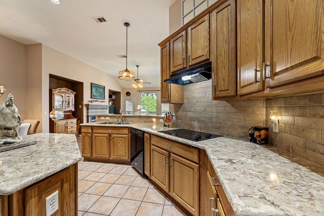 Kitchen featuring black appliances, a sink, under cabinet range hood, brown cabinets, and a peninsula | Image 15