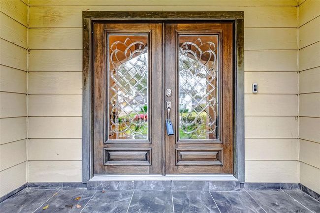 Rich wood double doors, adorned with leaded glass panels, create an inviting yet sophisticated entrance. The covered entryway offers shelter and an elegant transition into the home. | Image 4