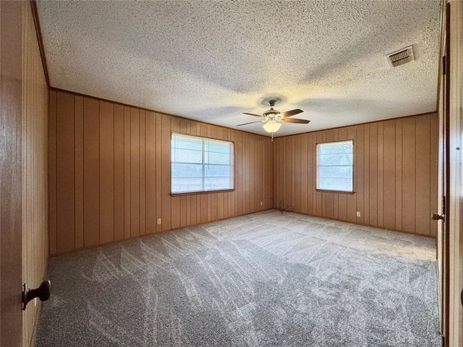 Carpeted empty room with ceiling fan, a textured ceiling, and wood walls | Image 24