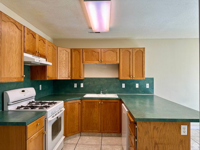 Kitchen featuring gas range gas stove, under cabinet range hood, a peninsula, dark countertops, and tasteful backsplash | Image 6