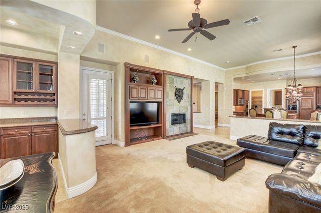 Living area with crown molding, visible vents, light carpet, baseboards, and ceiling fan with notable chandelier | Image 13