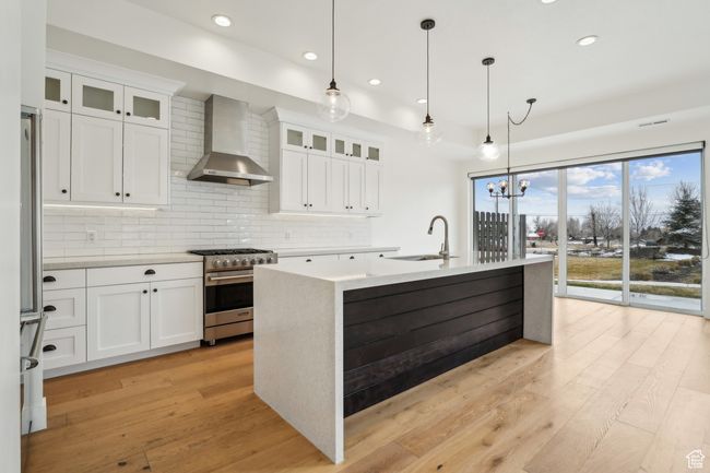 Kitchen with a sink, wall chimney range hood, light wood-type flooring, and stainless steel appliances | Image 7