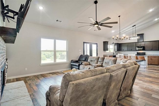 Living room with ceiling fan with notable chandelier, a stone fireplace, high vaulted ceiling, wood-type flooring, and sink | Image 5