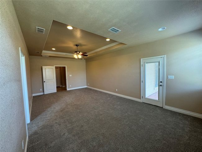 Empty room featuring a raised ceiling, visible vents, and dark carpet | Image 9