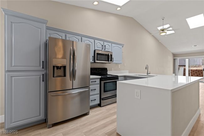 Kitchen with a skylight, stainless steel appliances, vaulted ceiling, a peninsula, and light wood finished floors | Image 9