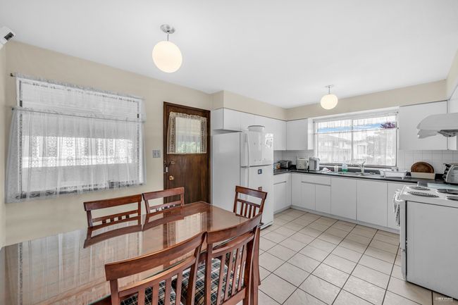 Kitchen featuring white appliances, dark countertops, white cabinetry, decorative light fixtures, and light tile patterned floors | Image 10