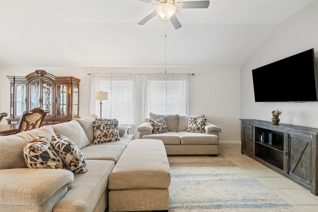 Living room with light tile patterned floors, baseboards, lofted ceiling, and ceiling fan | Image 10