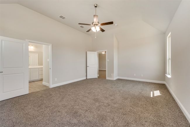 Primary bedroom with ceiling fan, light colored carpet, ensuite bathroom, and high vaulted ceiling | Image 17