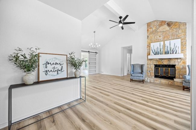 Unfurnished living room with a barn door, a ceiling fan, a stone fireplace, and high vaulted ceiling | Image 4