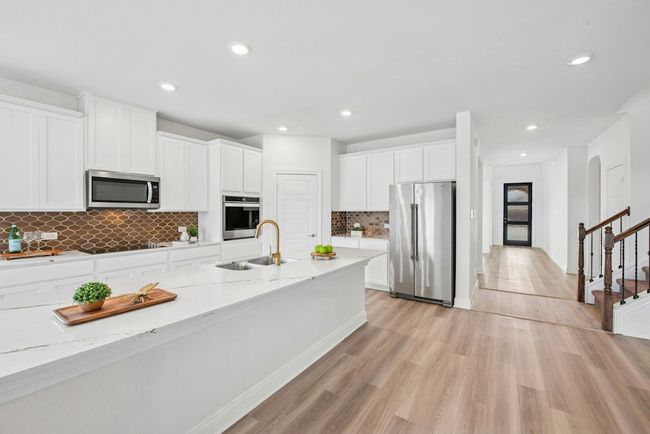 Kitchen featuring stainless steel appliances, kitchen island, white cabinets, backsplash, and light quartz countertops | Image 5
