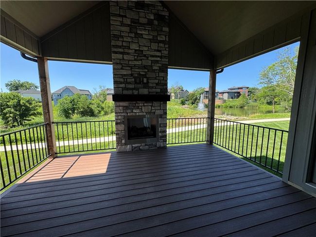 Wooden deck featuring an outdoor stone fireplace, a lawn, and a residential view | Image 10