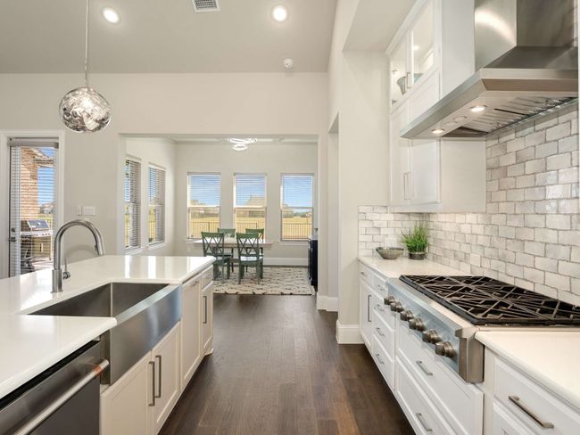 The kitchen is a culinary masterpiece, featuring an expansive island perfect for entertaining, quartz countertops, sleek white cabinetry with glass display fronts, an apron-front farm sink, and high-end stainless-steel appliances, including a six-burner gas cooktop and double convection oven. | Image 6