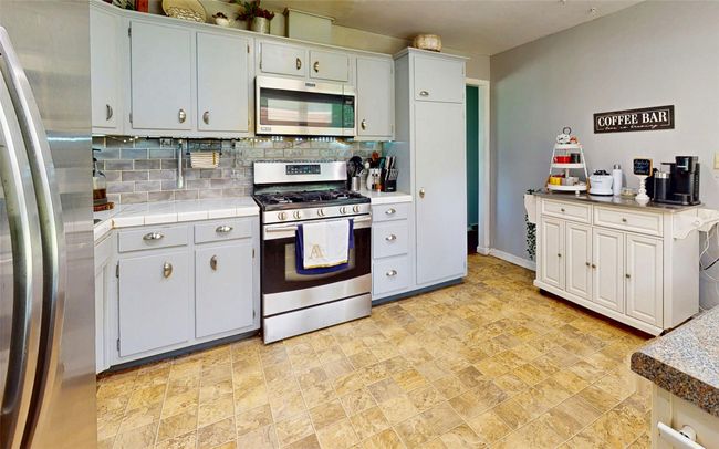Kitchen featuring stainless steel appliances, stone finish floors, tasteful backsplash, baseboards, and tile countertops | Image 19