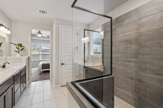 Full bath featuring double vanity, tiled shower, ensuite bath, tile patterned floors, and a ceiling fan | Image 21