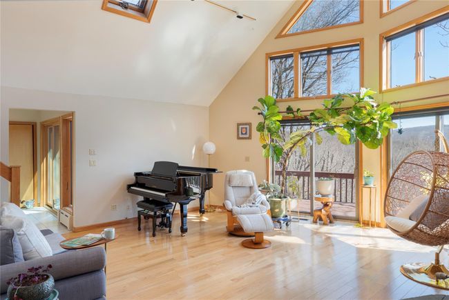 Living area featuring high vaulted ceiling, a skylight, a baseboard radiator, baseboards, and wood finished floors | Image 15