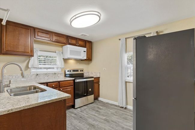 Kitchen with visible vents, appliances with stainless steel finishes, a sink, light stone countertops, and light wood-type flooring | Image 10