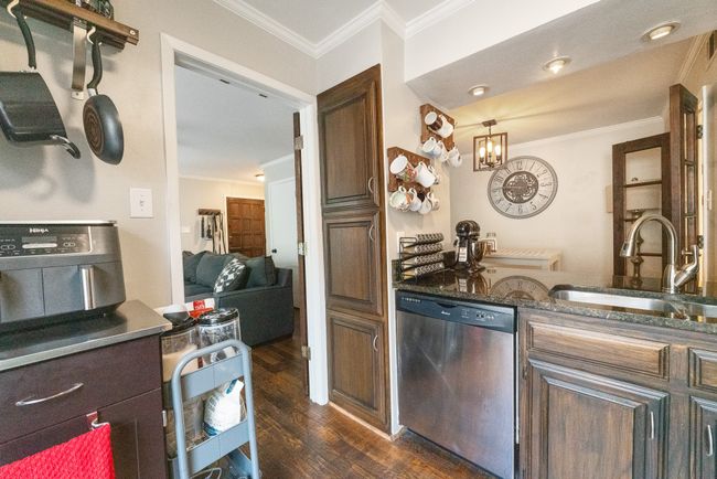 Kitchen featuring stainless steel dishwasher, a sink, crown molding, and dark wood-style floors | Image 6