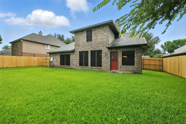 Rear view of property with brick siding, a fenced backyard, a chimney, and roof with shingles | Image 34