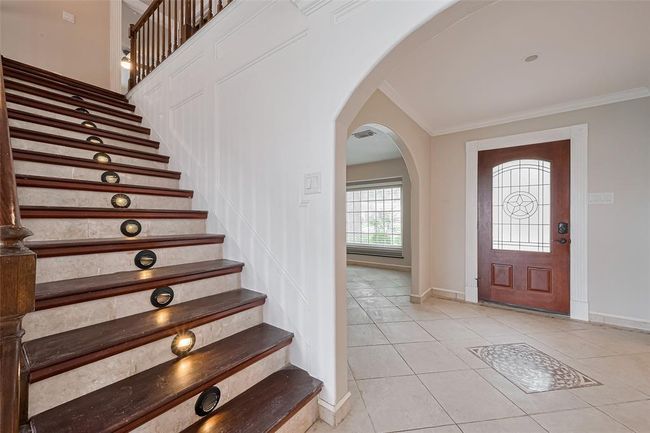 This beautifully detailed staircase features dark wood steps accented by stone tile risers and built-in step lighting—creating both safety and style. Wainscoting and classic trimwork complete the elegant entryway. | Image 7