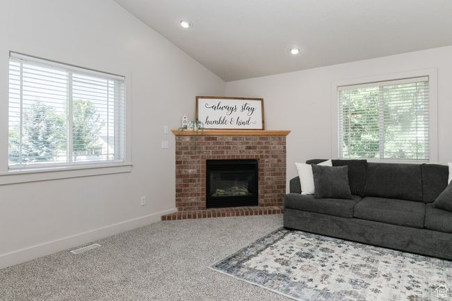Carpeted living room featuring healthy amount of natural light, lofted ceiling, a fireplace, and recessed lighting | Image 6