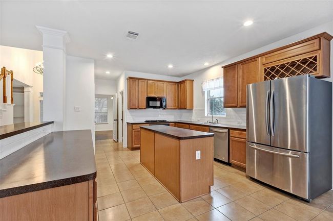 Modern kitchen with stainless steel appliances, wooden cabinetry, and a central island. Features a wine rack, ample counter space, and natural light from a window above the sink. | Image 5
