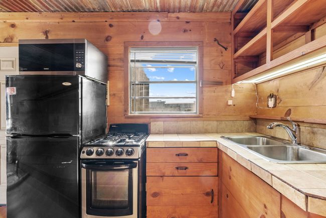 Kitchen with stainless steel gas range, freestanding refrigerator, tile countertops, a sink, and wood walls | Image 19
