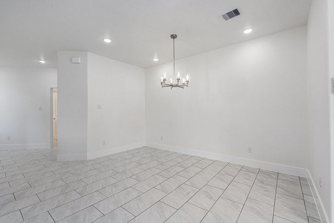 This photo shows a bright, open dining area with light tiled flooring and neutral walls. It features a modern chandelier and recessed lighting, creating a clean, inviting space. | Image 19