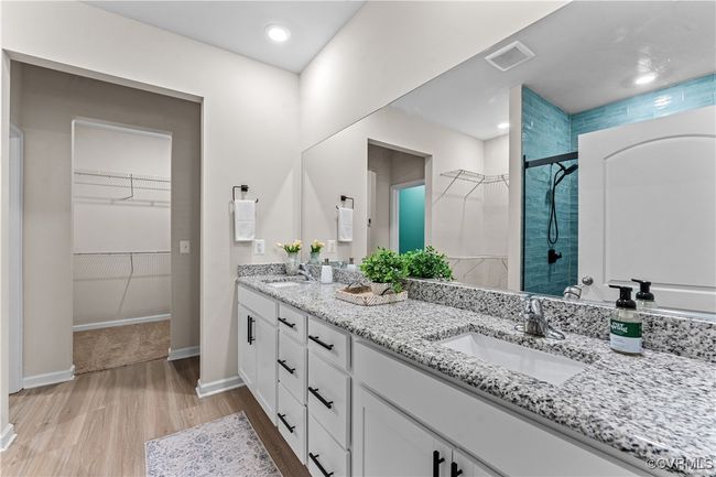Bathroom with wood finished floors, a stall shower, double vanity, a walk in closet, and baseboards | Image 32