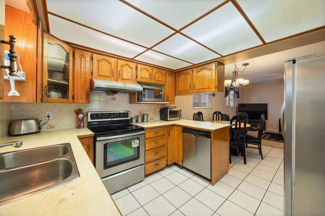 Kitchen with stainless steel appliances, under cabinet range hood, light countertops, a sink, and a peninsula | Image 21