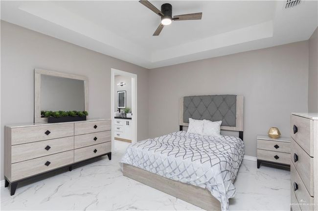 Bedroom featuring light marble finish flooring, a raised ceiling, ensuite bathroom, and baseboards | Image 7