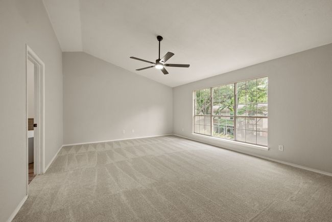The primary bedroom is generously sized with vaulted ceilings, large windows providing abundant natural light, and a modern ceiling fan. | Image 22