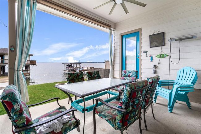 This photo showcases a charming covered patio with colorful seating and a glass-top table, perfect for relaxing. The patio overlooks a serene waterfront, offering a picturesque view of the water and docks, ideal for enjoying outdoor living. | Image 25