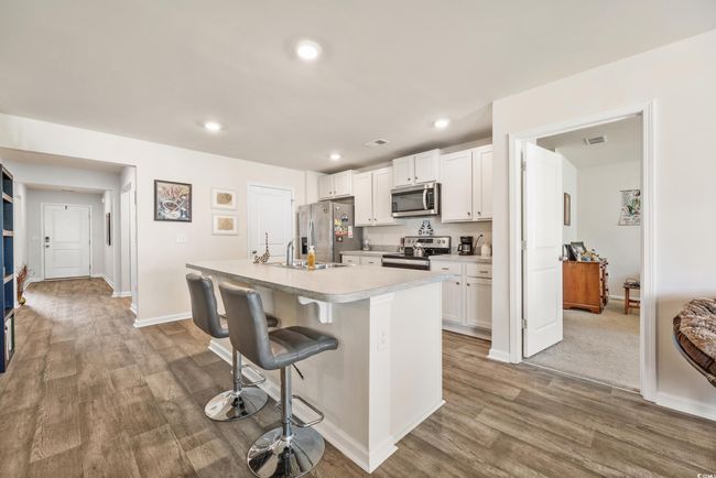 Kitchen with stainless steel appliances, light wood-style flooring, light countertops, white cabinetry, and an island with sink | Image 15
