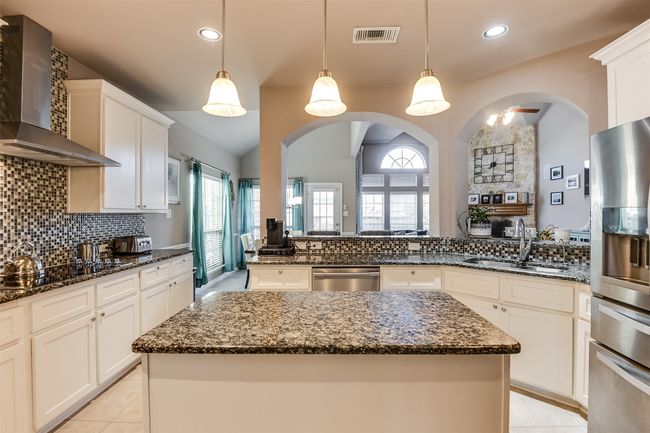Kitchen featuring stainless steel appliances, sink, wall chimney range hood, a center island, and hanging light fixtures | Image 19