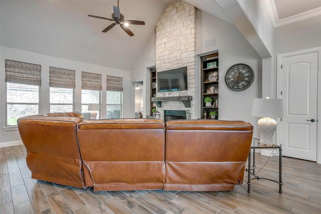 Living room featuring healthy amount of natural light, ceiling fan, a fireplace, high vaulted ceiling, and wood finish floors | Image 5