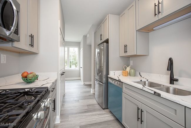 Kitchen featuring light stone countertops, light wood-type flooring, gray cabinetry, stainless steel appliances, and sink | Image 16