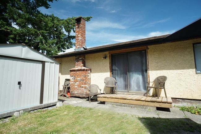 Rear view of property with stucco siding, a shed, a wooden deck, a yard, and a chimney | Image 5