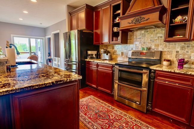 Kitchen with reddish brown cabinets, dark wood finished floors, custom exhaust hood, and stainless steel appliances | Image 12